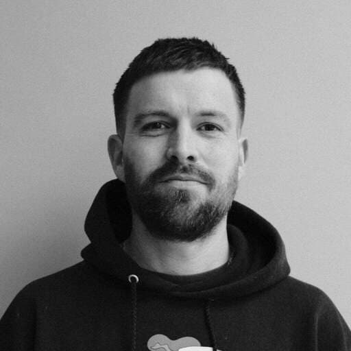 Black and white headshot of a bearded man with short hair, wearing a hoodie.