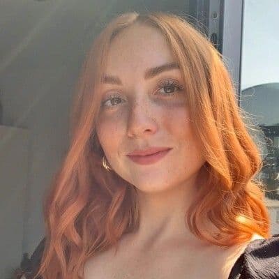 A young woman with wavy reddish-orange hair and freckles smiles softly.