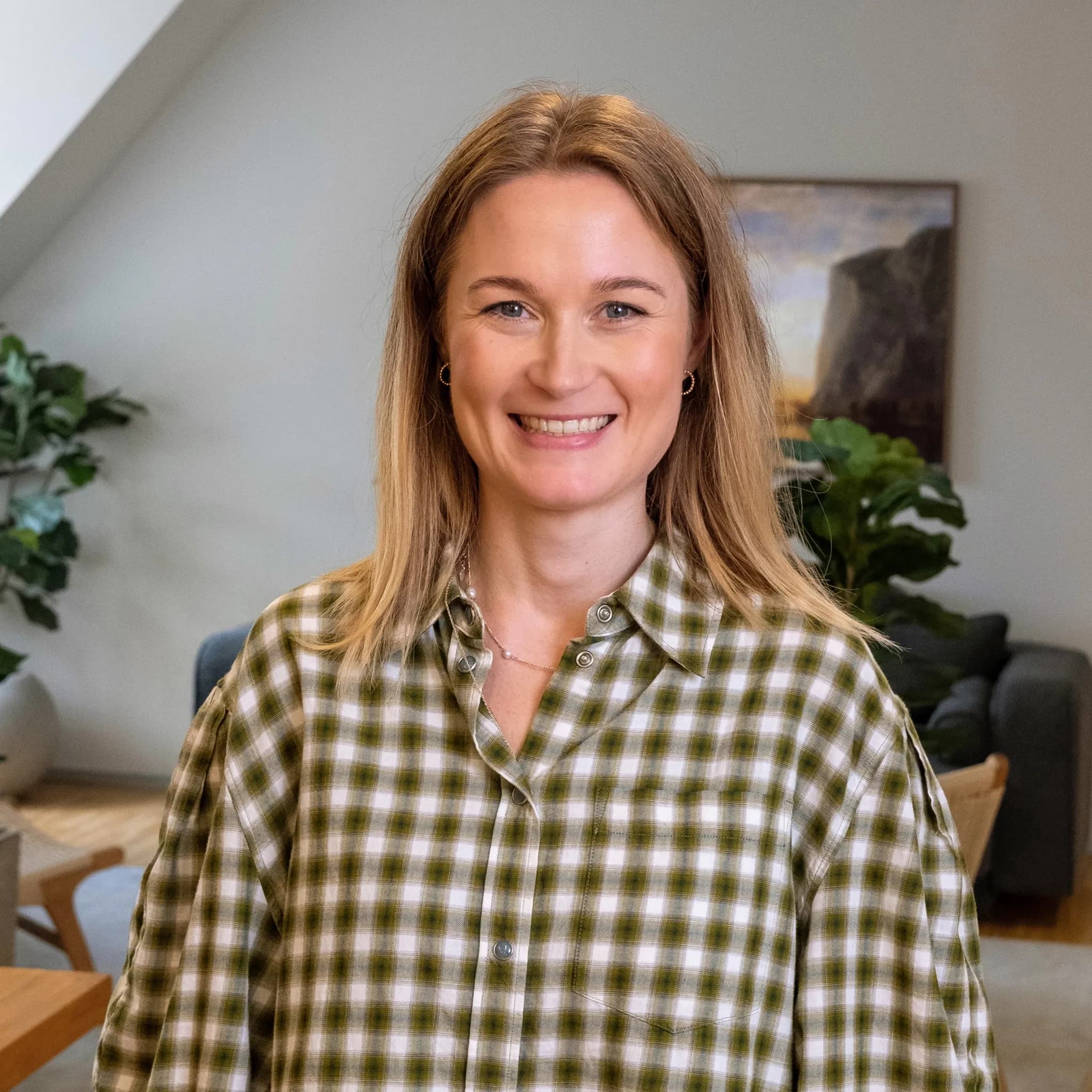 A smiling blonde woman in a green plaid shirt.